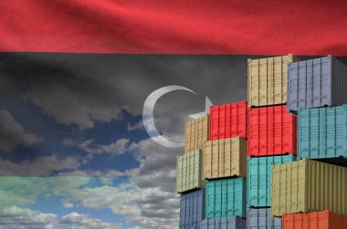 Libya flag and big stack of shipping cargo containers in docks with sky background close up clipart