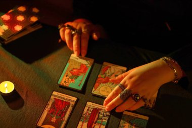 KYIV, UKRAINE - 10 Temmuz 2024 Tarot okuyucusu tarot kartı seçiyor. Karanlık odada mum ışığı. Tarot okuyucusu veya falcı okuma ve tahmin yakın yakın