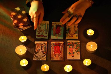KYIV, UKRAINE - 10 Temmuz 2024 Tarot okuyucusu tarot kartı seçiyor. Karanlık odada mum ışığı. Tarot okuyucusu veya falcı okuma ve tahmin yakın yakın