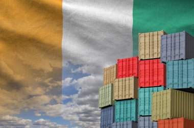 Ivory Coast flag and big stack of shipping cargo containers in docks with sky background close up clipart