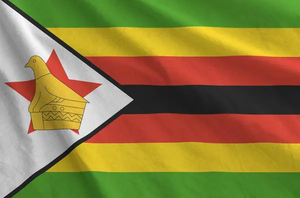 stock image Zimbabwe flag depicted on folded wavy fabric of old cloth close up