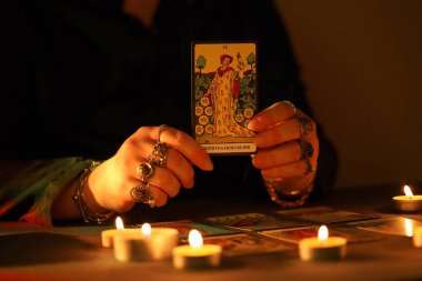 KYIV, UKRAINE - 10 Temmuz 2024 Tarot okuyucusu tarot kartı seçiyor. Karanlık odada mum ışığı. Tarot okuyucusu veya falcı okuma ve tahmin yakın yakın