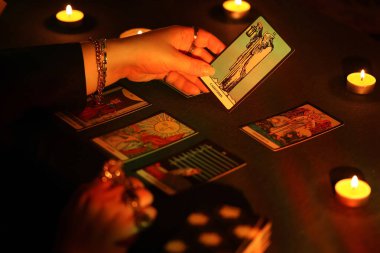 KYIV, UKRAINE - 10 Temmuz 2024 Tarot okuyucusu tarot kartı seçiyor. Karanlık odada mum ışığı. Tarot okuyucusu veya falcı okuma ve tahmin yakın yakın