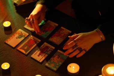 KYIV, UKRAINE - 10 Temmuz 2024 Tarot okuyucusu tarot kartı seçiyor. Karanlık odada mum ışığı. Tarot okuyucusu veya falcı okuma ve tahmin yakın yakın