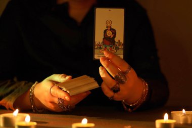 KYIV, UKRAINE - 10 Temmuz 2024 Tarot okuyucusu tarot kartı seçiyor. Karanlık odada mum ışığı. Tarot okuyucusu veya falcı okuma ve tahmin yakın yakın