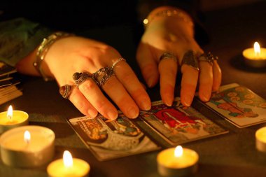 KYIV, UKRAINE - 10 Temmuz 2024 Tarot okuyucusu tarot kartı seçiyor. Karanlık odada mum ışığı. Tarot okuyucusu veya falcı okuma ve tahmin yakın yakın