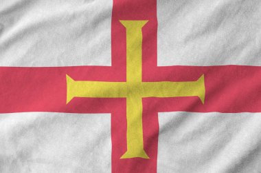 Guernsey flag depicted on folded wavy fabric of old cloth close up clipart