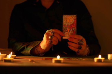 KYIV, UKRAINE - 10 Temmuz 2024 Tarot okuyucusu tarot kartı seçiyor. Karanlık odada mum ışığı. Tarot okuyucusu veya falcı okuma ve tahmin yakın yakın