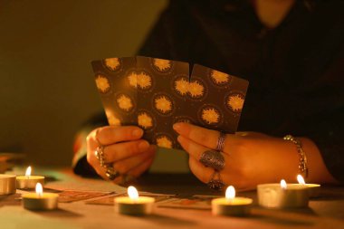 KYIV, UKRAINE - 10 Temmuz 2024 Tarot okuyucusu tarot kartı seçiyor. Karanlık odada mum ışığı. Tarot okuyucusu veya falcı okuma ve tahmin yakın yakın