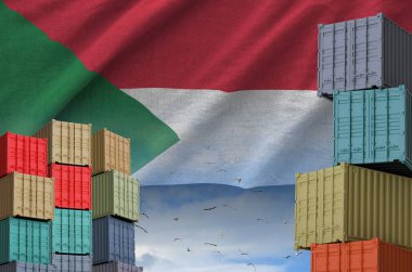 Sudan flag and big stack of shipping cargo containers in docks with sky background close up clipart