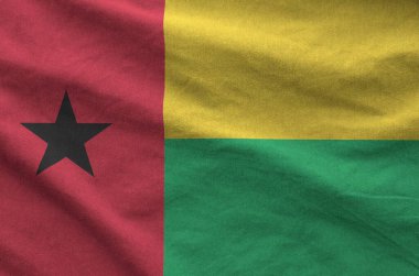 Guinea Bissau flag depicted on folded wavy fabric of old cloth close up clipart