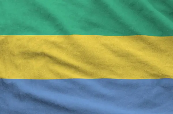 stock image Gabon flag depicted on folded wavy fabric of old cloth close up