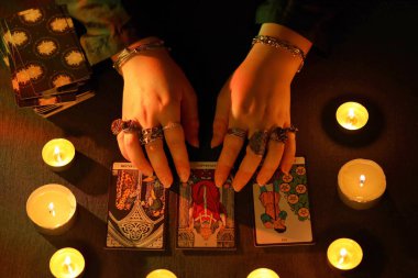 KYIV, UKRAINE - 10 Temmuz 2024 Tarot okuyucusu tarot kartı seçiyor. Karanlık odada mum ışığı. Tarot okuyucusu veya falcı okuma ve tahmin yakın yakın