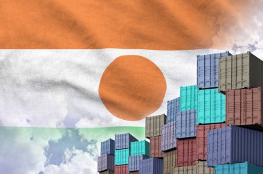 Niger flag and big stack of shipping cargo containers in docks with sky background close up clipart