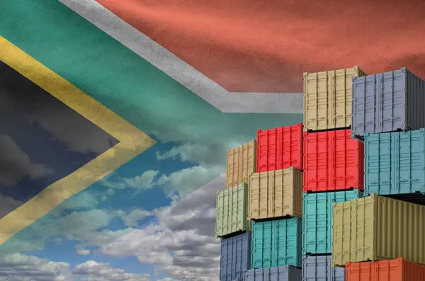 stock image South Africa flag and big stack of shipping cargo containers in docks with sky background close up