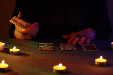 KYIV, UKRAINE - 10 Temmuz 2024 Tarot okuyucusu tarot kartı seçiyor. Karanlık odada mum ışığı. Tarot okuyucusu veya falcı okuma ve tahmin yakın yakın