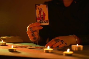 KYIV, UKRAINE - 10 Temmuz 2024 Tarot okuyucusu tarot kartı seçiyor. Karanlık odada mum ışığı. Tarot okuyucusu veya falcı okuma ve tahmin yakın yakın