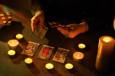 KYIV, UKRAINE - 10 Temmuz 2024 Tarot okuyucusu tarot kartı seçiyor. Karanlık odada mum ışığı. Tarot okuyucusu veya falcı okuma ve tahmin yakın yakın