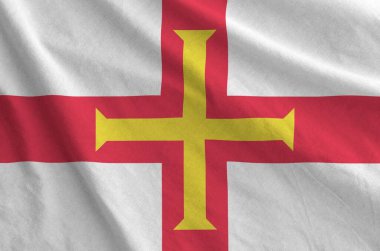 Guernsey flag depicted on folded wavy fabric of old cloth close up clipart