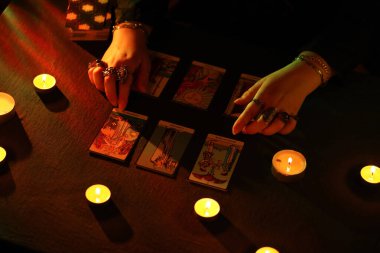 KYIV, UKRAINE - 10 Temmuz 2024 Tarot okuyucusu tarot kartı seçiyor. Karanlık odada mum ışığı. Tarot okuyucusu veya falcı okuma ve tahmin yakın yakın