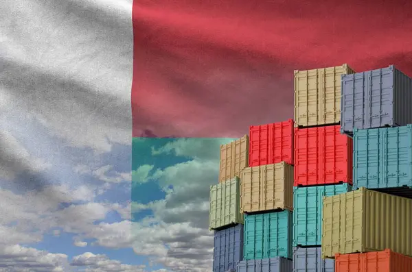 stock image Madagascar flag and big stack of shipping cargo containers in docks with sky background close up