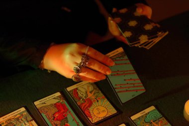 KYIV, UKRAINE - 10 Temmuz 2024 Tarot okuyucusu tarot kartı seçiyor. Karanlık odada mum ışığı. Tarot okuyucusu veya falcı okuma ve tahmin yakın yakın
