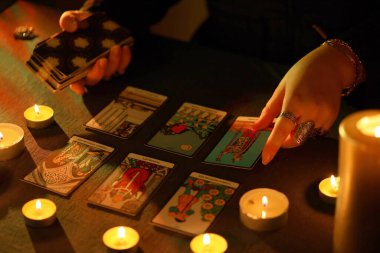 KYIV, UKRAINE - 10 Temmuz 2024 Tarot okuyucusu tarot kartı seçiyor. Karanlık odada mum ışığı. Tarot okuyucusu veya falcı okuma ve tahmin yakın yakın