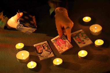 KYIV, UKRAINE - 10 Temmuz 2024 Tarot okuyucusu tarot kartı seçiyor. Karanlık odada mum ışığı. Tarot okuyucusu veya falcı okuma ve tahmin yakın yakın