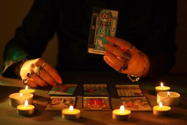 KYIV, UKRAINE - 10 Temmuz 2024 Tarot okuyucusu tarot kartı seçiyor. Karanlık odada mum ışığı. Tarot okuyucusu veya falcı okuma ve tahmin yakın yakın
