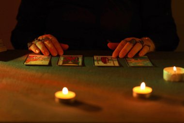 KYIV, UKRAINE - 10 Temmuz 2024 Tarot okuyucusu tarot kartı seçiyor. Karanlık odada mum ışığı. Tarot okuyucusu veya falcı okuma ve tahmin yakın yakın