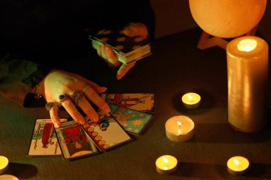 KYIV, UKRAINE - 10 Temmuz 2024 Tarot okuyucusu tarot kartı seçiyor. Karanlık odada mum ışığı. Tarot okuyucusu veya falcı okuma ve tahmin yakın yakın