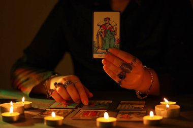 KYIV, UKRAINE - 10 Temmuz 2024 Tarot okuyucusu tarot kartı seçiyor. Karanlık odada mum ışığı. Tarot okuyucusu veya falcı okuma ve tahmin yakın yakın