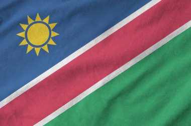 Namibia flag depicted on folded wavy fabric of old cloth close up clipart