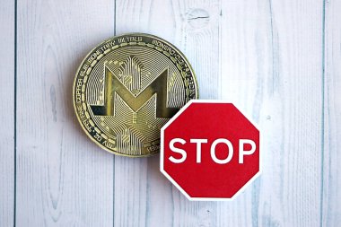 KYIV, UKRAINE - AUGUST 17, 2024 Monero XMR coin and red paper stop sign on wooden background close up clipart