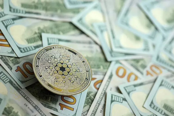 stock image KYIV, UKRAINE - AUGUST 17, 2024 Cardano ADA coin on big amount of hundred US dollar bills close up