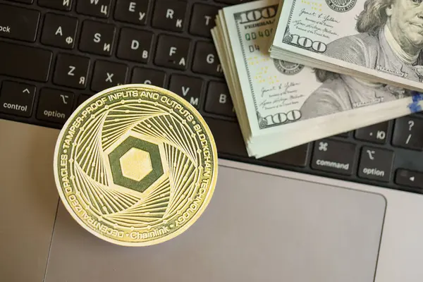 stock image KYIV, UKRAINE - AUGUST 17, 2024 Chainlink LINK coin with big amount of hundred US dollar bills on laptop surface close up