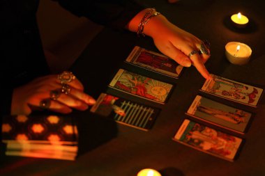 KYIV, UKRAINE - 10 Temmuz 2024 Tarot okuyucusu tarot kartı seçiyor. Karanlık odada mum ışığı. Tarot okuyucusu veya falcı okuma ve tahmin yakın yakın