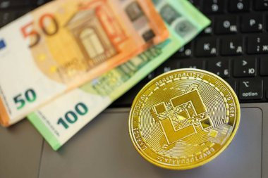 KYIV, UKRAINE - 17 AĞUSTOS 2024 Binance BNB madeni parası ve dizüstü bilgisayarda büyük miktarda Avro banknotları