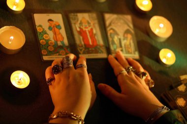 KYIV, UKRAINE - 10 Temmuz 2024 Tarot okuyucusu tarot kartı seçiyor. Karanlık odada mum ışığı. Tarot okuyucusu veya falcı okuma ve tahmin yakın yakın