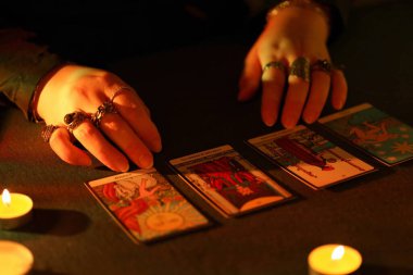 KYIV, UKRAINE - 10 Temmuz 2024 Tarot okuyucusu tarot kartı seçiyor. Karanlık odada mum ışığı. Tarot okuyucusu veya falcı okuma ve tahmin yakın yakın