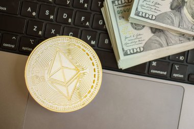 KYIV, UKRAINE - 17 AĞUSTOS 2024 Ethereum ETH madeni parasıyla dizüstü bilgisayar yüzeyinde büyük miktarlarda Amerikan Doları var.