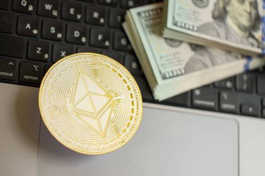 KYIV, UKRAINE - 17 AĞUSTOS 2024 Ethereum ETH madeni parasıyla dizüstü bilgisayar yüzeyinde büyük miktarlarda Amerikan Doları var.