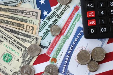 Amerikan doları para faturaları, sosyal güvenlik numarası ve Amerikan bayrağındaki hesap makinesi yakın plan. Vergi ödeme ve sigorta kavramı