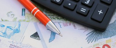 Arjantin Pezosu 'nun büyük miktarlarda para banknotları kalem ve hesap makinesiyle masanın üzerinde duruyor. Maliye ve vergi ödeme kavramı