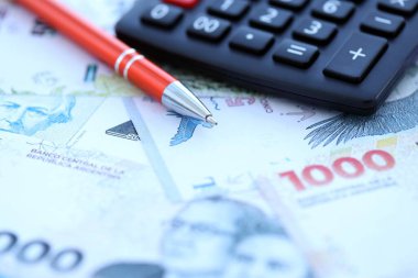 Arjantin Pezosu 'nun büyük miktarlarda para banknotları kalem ve hesap makinesiyle masanın üzerinde duruyor. Maliye ve vergi ödeme kavramı