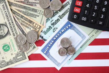 Amerikan doları para faturaları, sosyal güvenlik numarası ve Amerikan bayrağındaki hesap makinesi yakın plan. Vergi ödeme ve sigorta kavramı