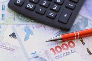 Arjantin Pezosu 'nun büyük miktarlarda para banknotları kalem ve hesap makinesiyle masanın üzerinde duruyor. Maliye ve vergi ödeme kavramı