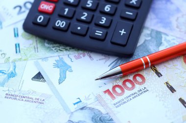 Arjantin Pezosu 'nun büyük miktarlarda para banknotları kalem ve hesap makinesiyle masanın üzerinde duruyor. Maliye ve vergi ödeme kavramı
