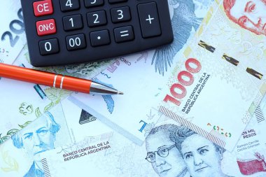 Arjantin Pezosu 'nun büyük miktarlarda para banknotları kalem ve hesap makinesiyle masanın üzerinde duruyor. Maliye ve vergi ödeme kavramı