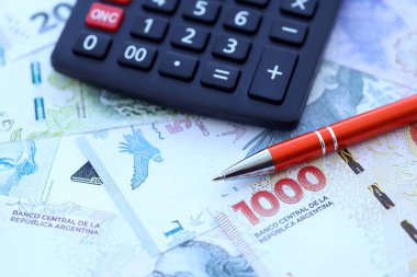 Arjantin Pezosu 'nun büyük miktarlarda para banknotları kalem ve hesap makinesiyle masanın üzerinde duruyor. Maliye ve vergi ödeme kavramı